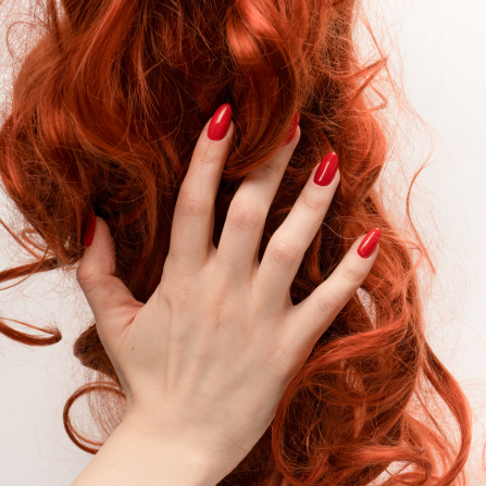 Une femme au vernis rouge tient ses cheveux rouges éclatants