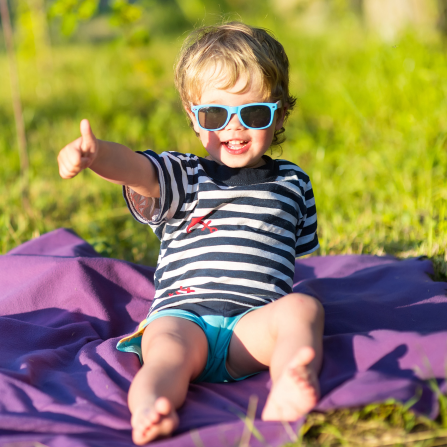 Un enfant assis dans l'herbe porte des lunettes de soleil et lève le pouce en l'air