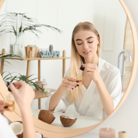 Une femme assise devant son miroir utilise de l'huile de coco pour ses cheveux