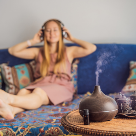 Une femme diffuse de l'huile essentielle en écoutant de la musique dans son canapé