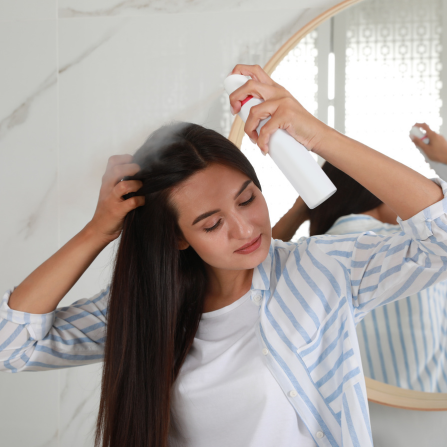 Une femme aux cheveux bruns et longs utilise un shampoing sec pour un coup de propre rapide