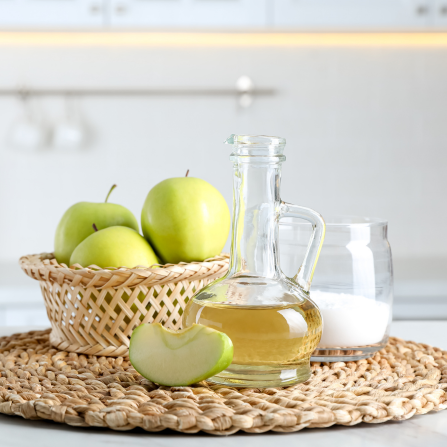 Une carafe de vinaigre de cidre de pomme et un pot de bicarbonate de soude pour la préparation d'un shampoing maison