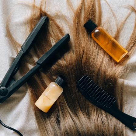 Un fer à lisser, un peigne et des produits capillaires posés sur des cheveux