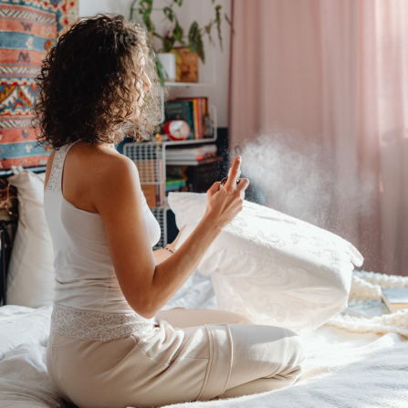 Une femme vaporise des huiles essentielles sur son oreiller et ses draps